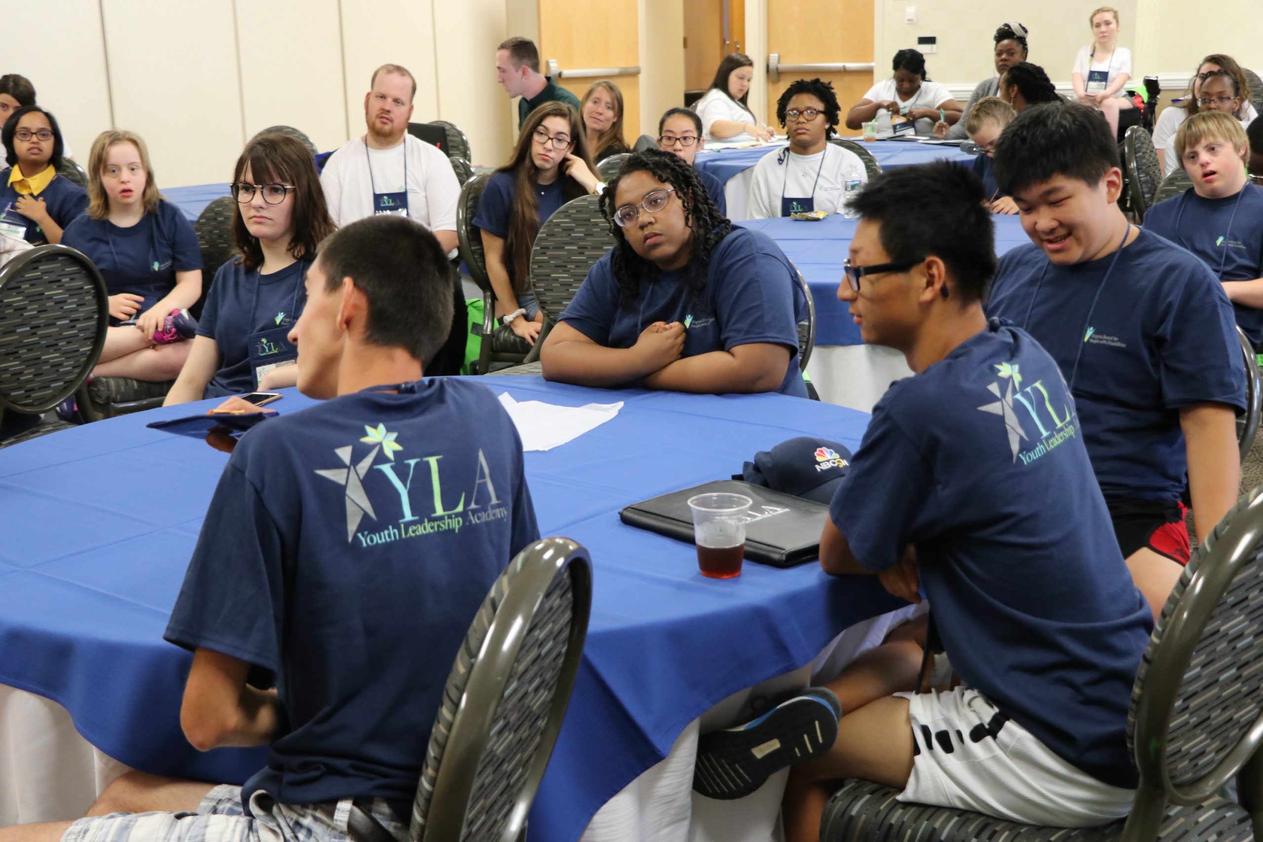 Students in matching YLA tee shirts sitting around a blue conference table